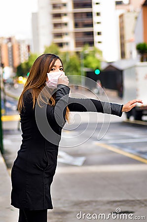 Young woman with protective mask on the street in the city with air pollution, asking for a taxi, city background Stock Photo