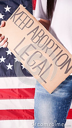 Young woman protester holds cardboard with Keep Abortion Legal sign against USA flag on background. Girl protesting against anti- Stock Photo