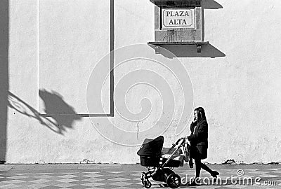 Young Woman Pushing Baby Buggy While Talking on Mobile Phone. Editorial Stock Photo