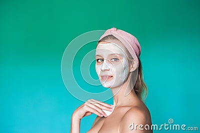 A young woman puts a white mask on her face with her hands. Beauty photo of a woman with a light mask on her face against a blue t Stock Photo