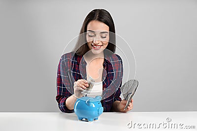 Young woman putting money into piggy bank at table on light grey background Stock Photo