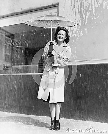 Young woman in a raincoat and umbrella standing in the rain Stock Photo