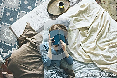 Young woman reading book on bed in loft room, slow life Stock Photo