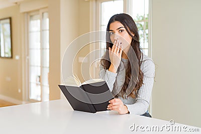 Young woman reading a book cover mouth with hand shocked with shame for mistake, expression of fear, scared in silence, secret Stock Photo