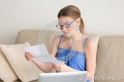 Young woman reading mail letter sitting with laptop on couch Stock Photo