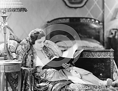 Young woman reclining in an armchair and reading a book in her bed room Stock Photo