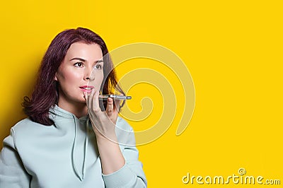 Young woman is recording an audio message on her smartphone. Horizontal studio shot on yellow background Stock Photo