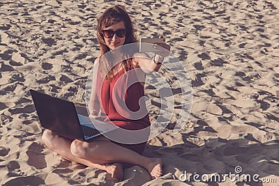 Young woman in red dress with computer and smartphone on the beach. Freelance and downshifting concept. Stock Photo