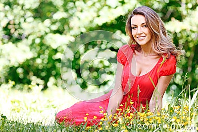 Young woman in red dress sitting on grass Stock Photo