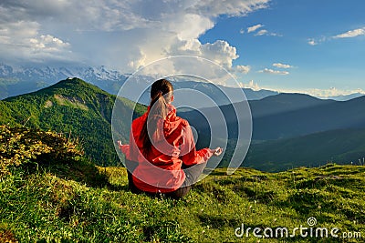 Young woman in red jacket sitting in yoga pose in mountains Stock Photo