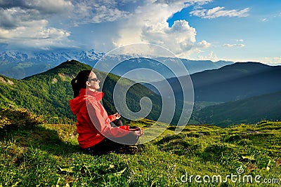 Young woman in red jacket sitting in yoga pose in mountains Stock Photo