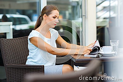 Young woman with red lips reads a newspaper sitting in a cafe Stock Photo