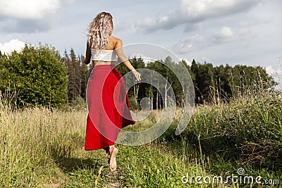 A young woman in a red skirt runs in the field. Back view. Power of nature Stock Photo