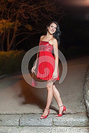 Young woman in red sleeveless dress walking in night park Stock Photo