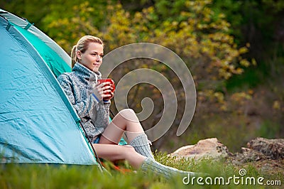 Young woman relaxing with a cup of tea near a tent against green Stock Photo