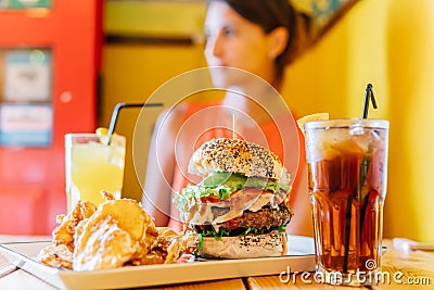 Young Woman In Restaurant Enjoying Tasty Juicy American Beef Burger Menu With Lettuce, Ketchup And Potato Chips Stock Photo