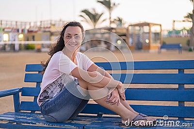 Young woman resting on bench. A woman with a beautiful smile on a blue bench. The concept of rest and happiness Stock Photo