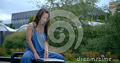 Young woman is resting in park alone, open notebook, sitting on bench Stock Photo