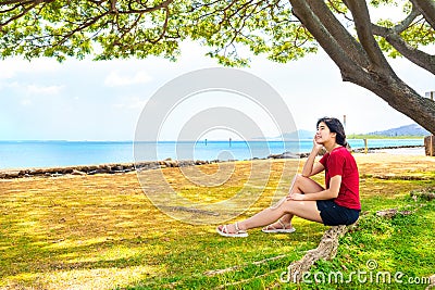 Young woman resting in shade of large canopy tree in Hawaii Stock Photo