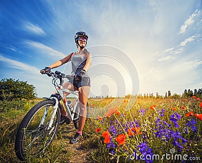 Young woman riding a bicycle on a blooming poppy meadow Stock Photo