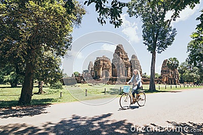 Young woman riding bicycle next to Pre Rup temple in Angkor Wat complex, Cambodia Stock Photo