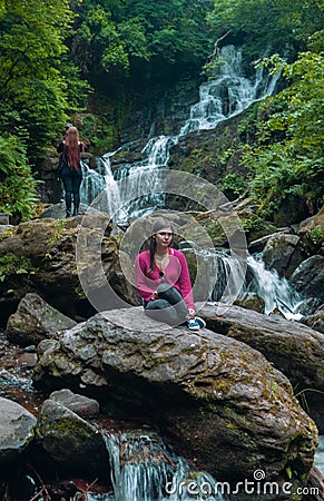 Young woman after a rock climb watching and exploring Torc Waterfall in the Killarney National Park, Ring of Kerry Tour, Ireland Stock Photo