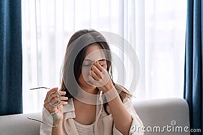 Young woman rubbing her eyes feel painful and take off her glasses sitting on sofa and rest one`s eyes at home Stock Photo