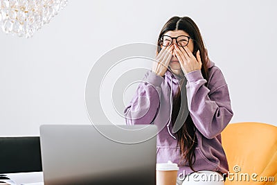 Young woman rubs her eyes after using glasses in front laptop. Eye pain or fatigue concept Stock Photo