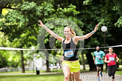 Young woman running in the crowd crossing the finish line. Stock Photo