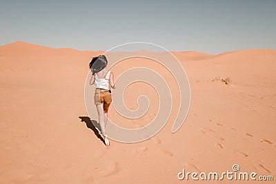 Young woman running through the sand dunes in the desert Stock Photo