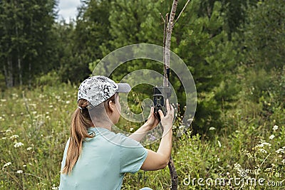 Young woman scientist zoologist sets camera trap for observing wild animals in forest to collect scientific data Environmental Stock Photo