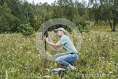 Young woman scientist zoologist sets camera trap for observing wild animals in forest to collect scientific data Environmental Stock Photo