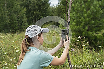 Young woman scientist zoologist sets camera trap for observing wild animals in forest to collect scientific data Environmental Stock Photo