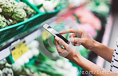 Young woman shopping purchase healthy food in supermarket blur background. Close up view girl buy products using smartphone in sto Stock Photo