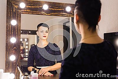 Young woman with short hair looking herself reflection in mirror Stock Photo