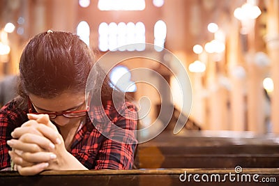 Young woman sits on a bench in the church and prays to God. Hands folded in prayer concept for faith Stock Photo