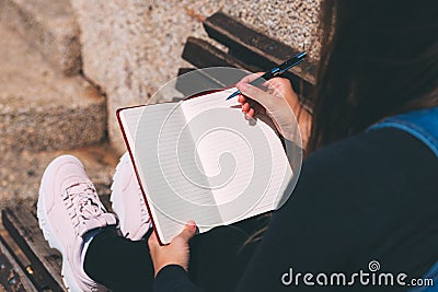 Young woman sits on bench in park with blank notebook and pen on her hands. Stock Photo