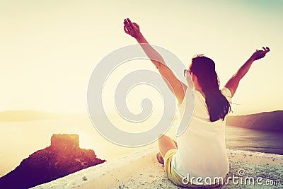 Young woman sits with hands up admiring Santorini, Greece Stock Photo