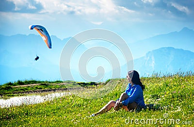 Young woman sits in the meadow and looks at the paraplane. Stock Photo