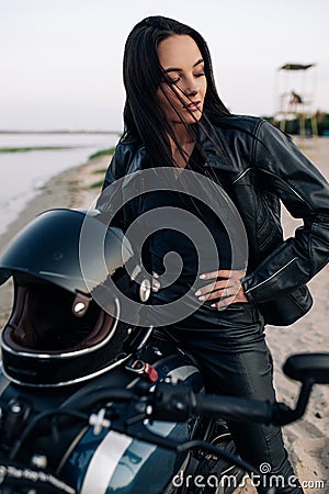 Young woman sits on motorbike on beach next coast of river Stock Photo