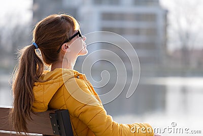 Young woman sitting alone on park bench relaxing on warm autumn day Stock Photo