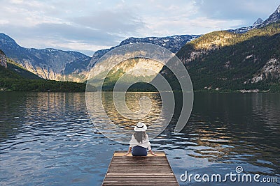 Young woman sitting alone on wooden pier, looking lake and mountain view in summer at Hallstatt, Austria Editorial Stock Photo