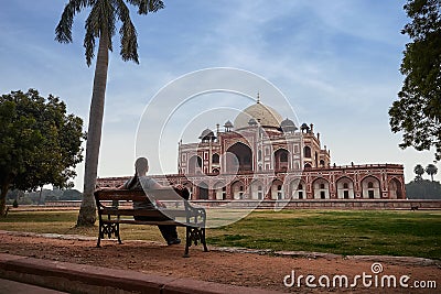 Young woman sitting at a bench and lookin to Humayun`s tomb in Delhi, India. Editorial Stock Photo