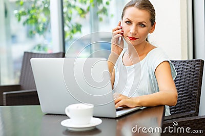 Young woman sitting in a cafe with a laptop and talking on the c Stock Photo