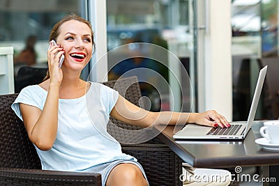 Young woman sitting in a cafe with a laptop and talking on the c Stock Photo