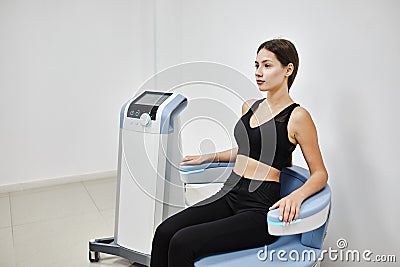 Young woman sitting on electromagnetic chair for stimulation of deep pelvic floor muscles and restoring neuromuscular control at Stock Photo