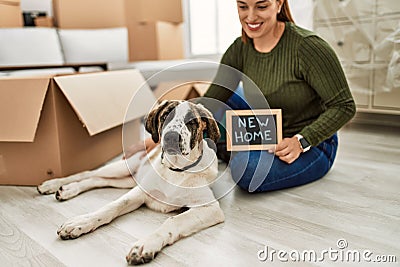 Young woman sitting on floor with dog holding new home blackboard message at home Stock Photo