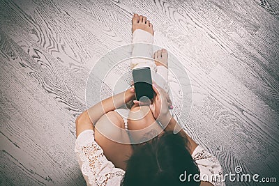 Young woman sitting on floor with smartphone, top view Stock Photo