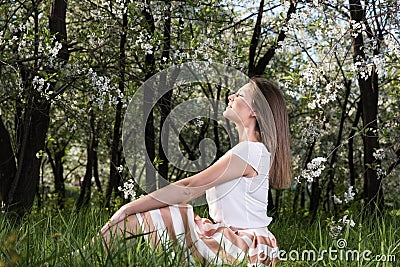 Young woman sitting on the grass in the lush garden and enjoying the sun Stock Photo