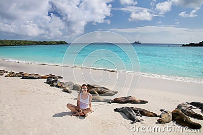 Young woman sitting with a group of Galapagos sea lions at Gardner Bay, Espanola Island, Galapagos National park, Ecuador Stock Photo